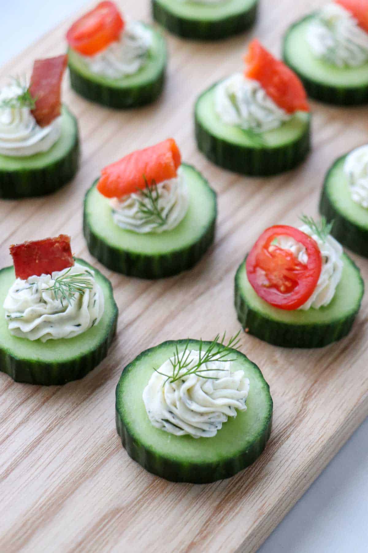 Cucumbers topped with cream cheese, dill, bacon, smoked salmon and tomato on a wooden board.