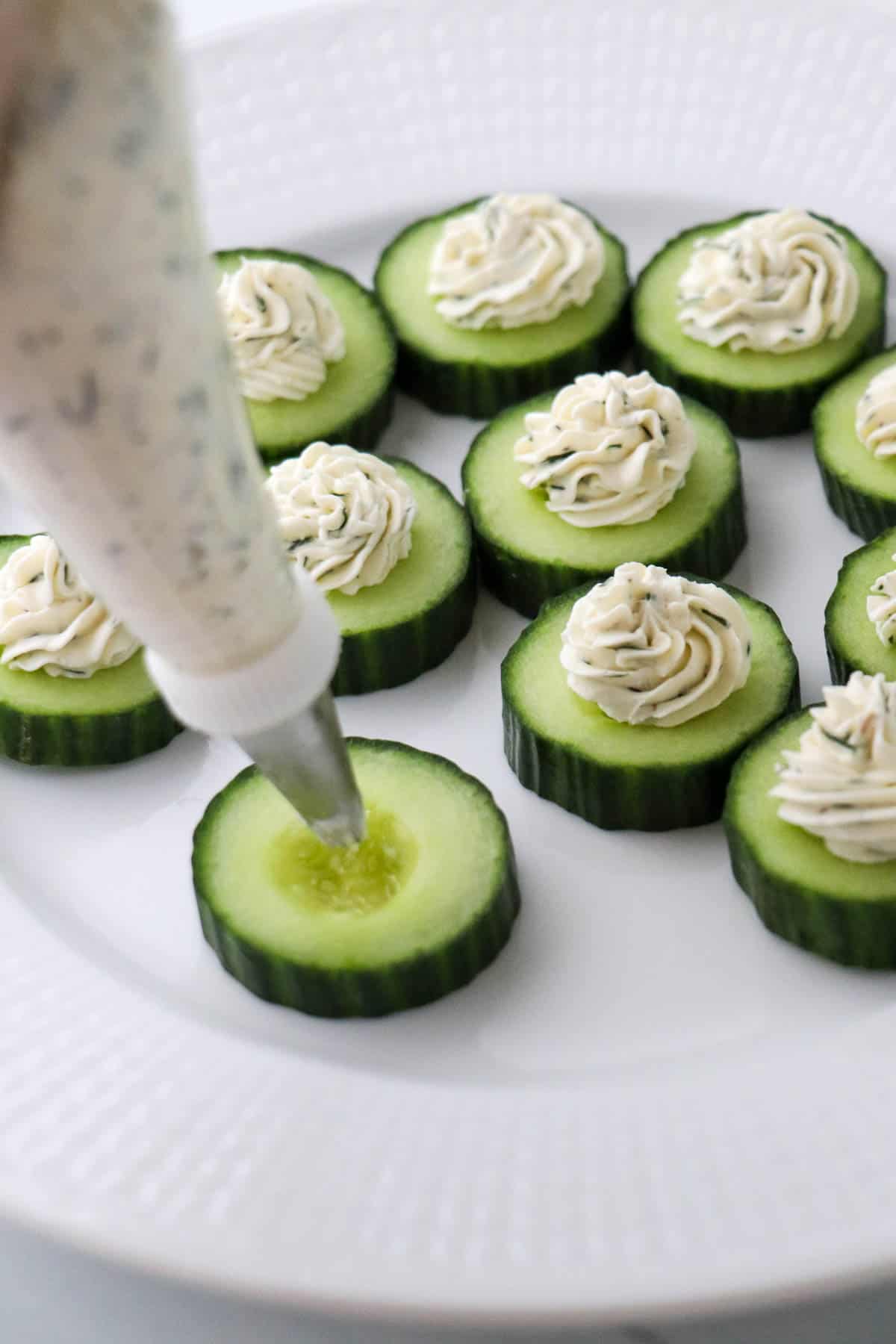 Person piping cream cheese onto cucumber rounds.