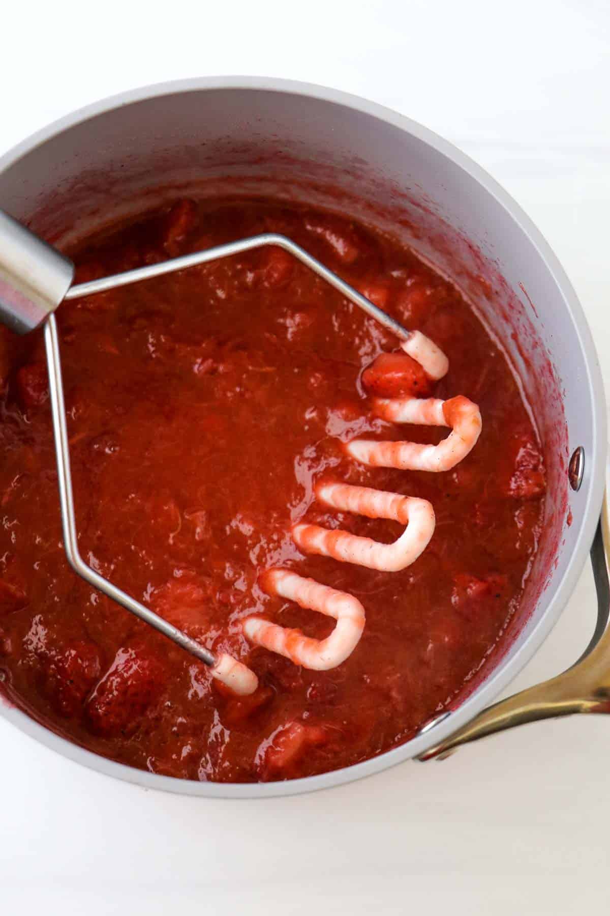 Potato masher in a saucepan with Strawberry Rhubarb Compote.