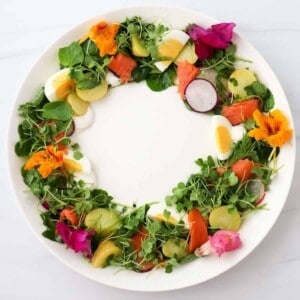 Midsummer Salad with greens, salmon, eggs and potatoes in a wreath shape on a white plate.