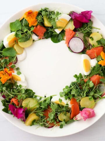 Midsummer Salad with greens, salmon, eggs and potatoes in a wreath shape on a white plate.