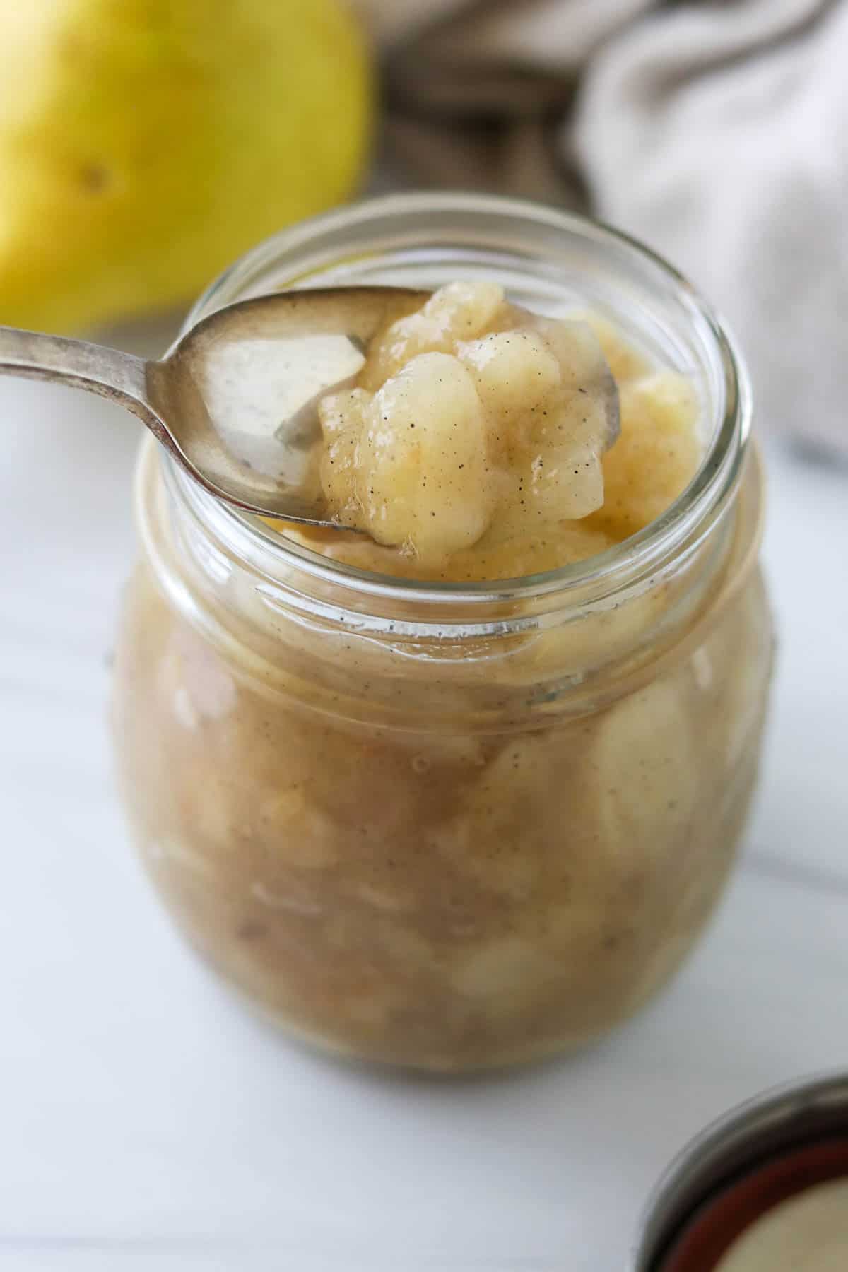 Spoonful of pear compote over a jar of it.