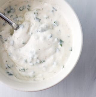 Close up of Horseradish Yogurt Sauce in a white bowl with a spoon.