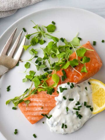 Overhead view of salmon, greens, Horseradish Yogurt Sauce and a lemon wedge on a plate next to a fork.