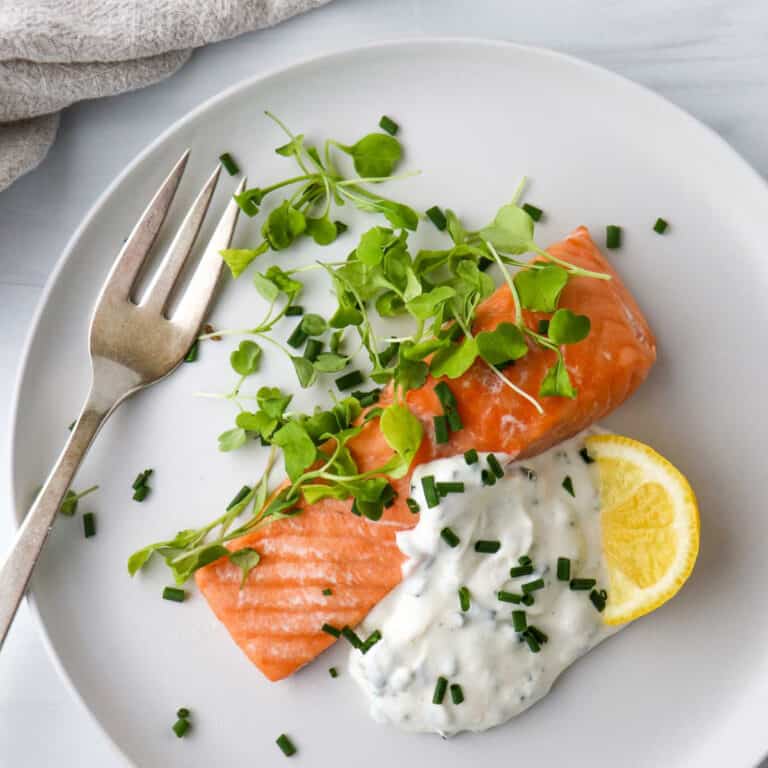 Overhead view of salmon, greens, Horseradish Yogurt Sauce and a lemon wedge on a plate next to a fork.