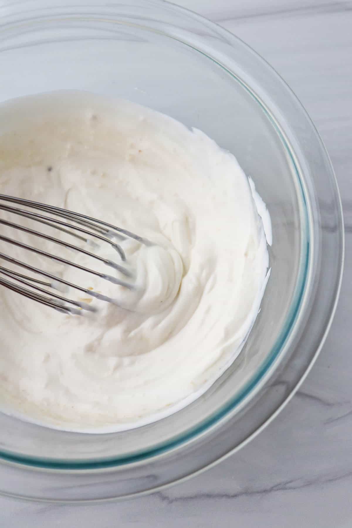 Horseradish Yogurt Sauce in a glass bowl with a whisk.