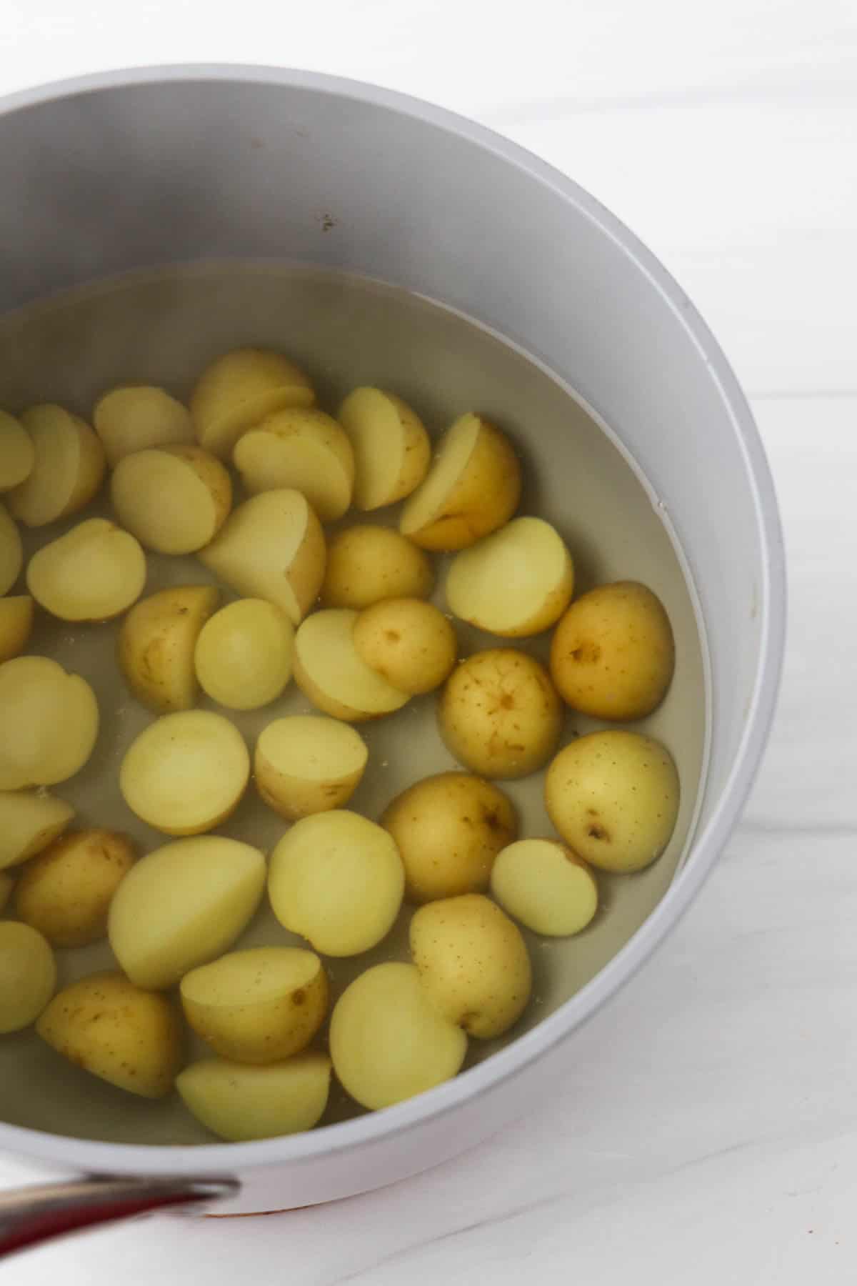 Halved new potatoes in water in saucepan.