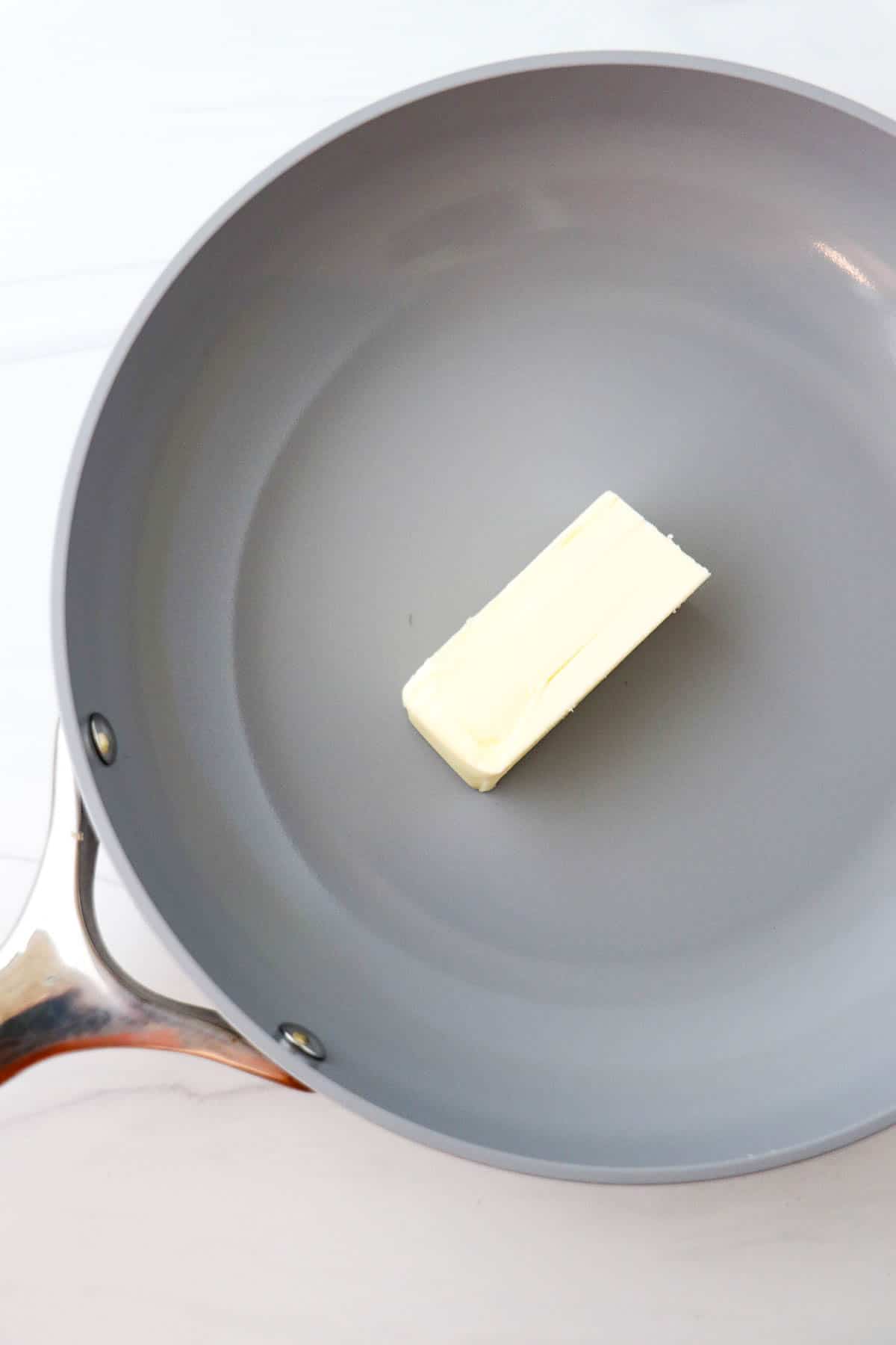 Stick of butter in a gray skillet.
