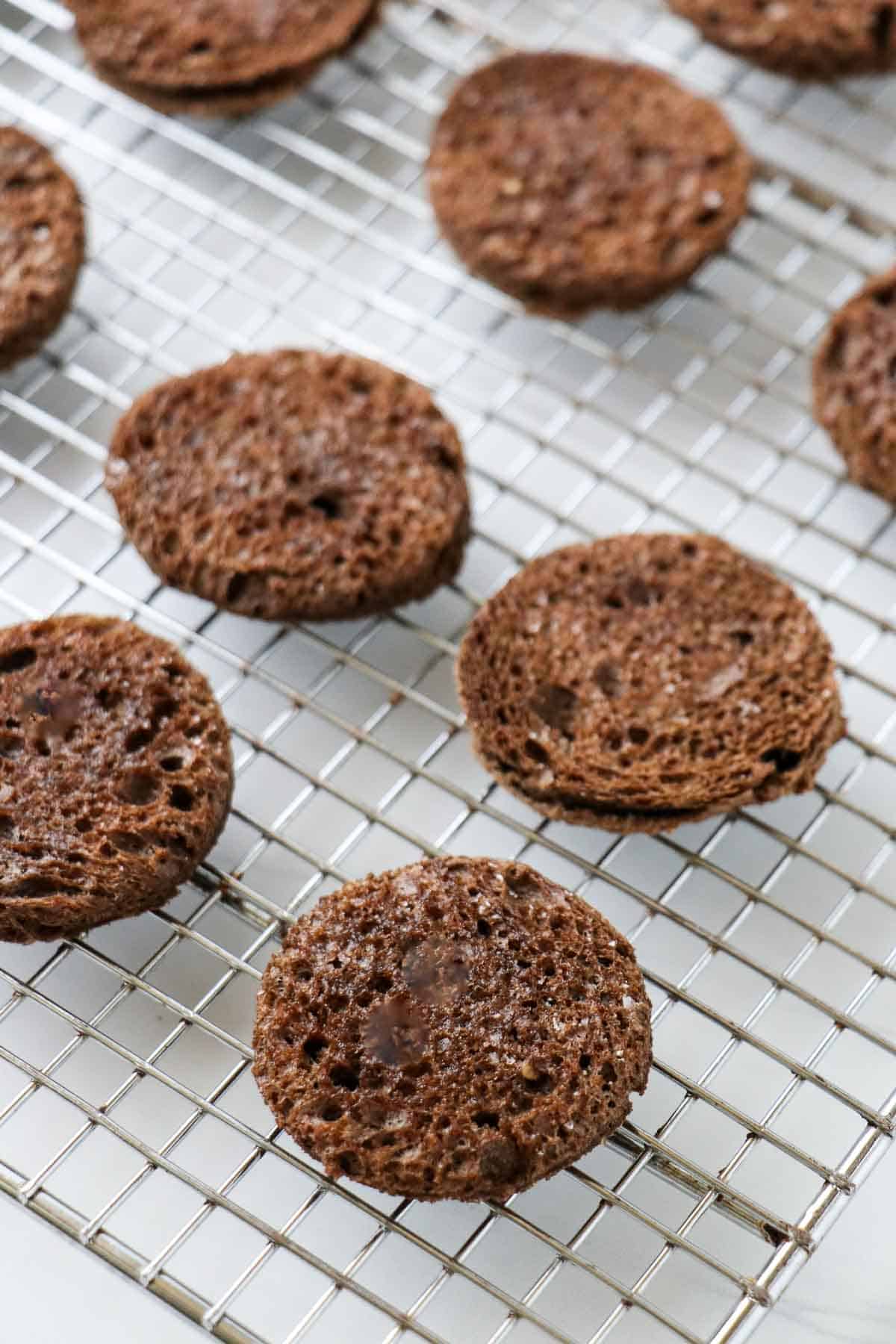 Toasted rye bread rounds on a metal cooling rack.