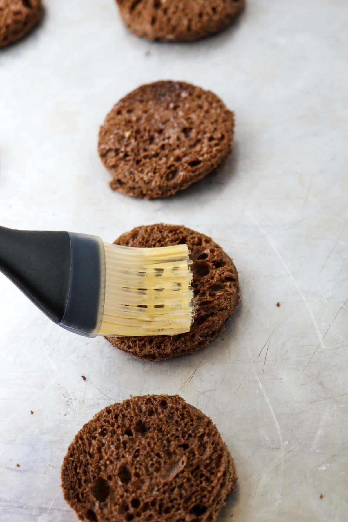 Brushing melted butter on rye bread rounds.