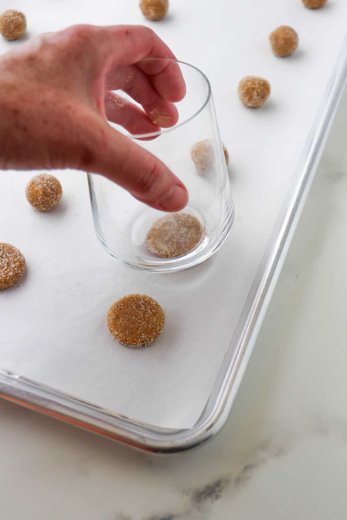Person pressing a glass down on Swedish Ginger Cookies dough balls.