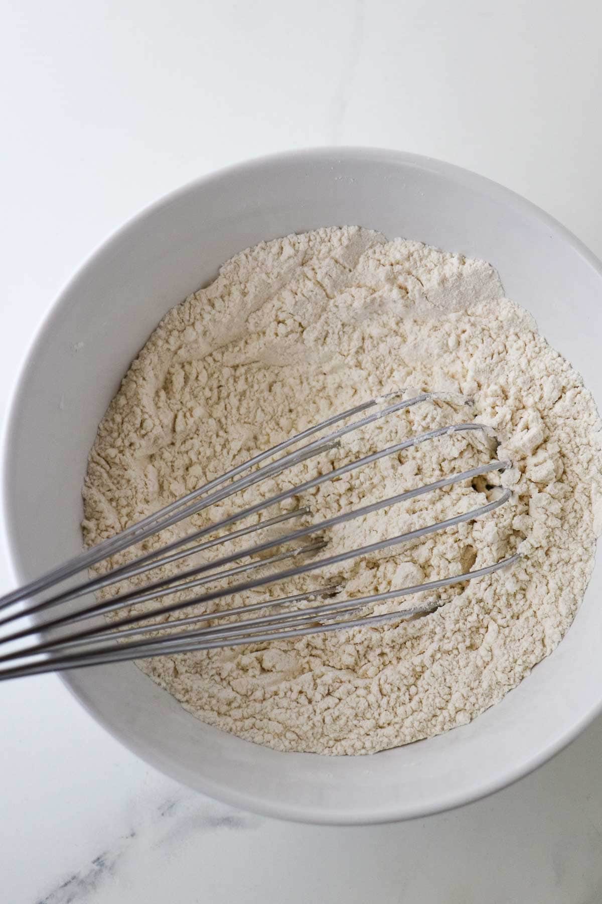 Dry ingredients in a white bowl with a whisk.