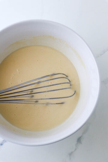 Krumkake batter in a white bowl with a whisk.