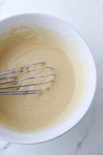Krumkake batter in a white bowl with a whisk.