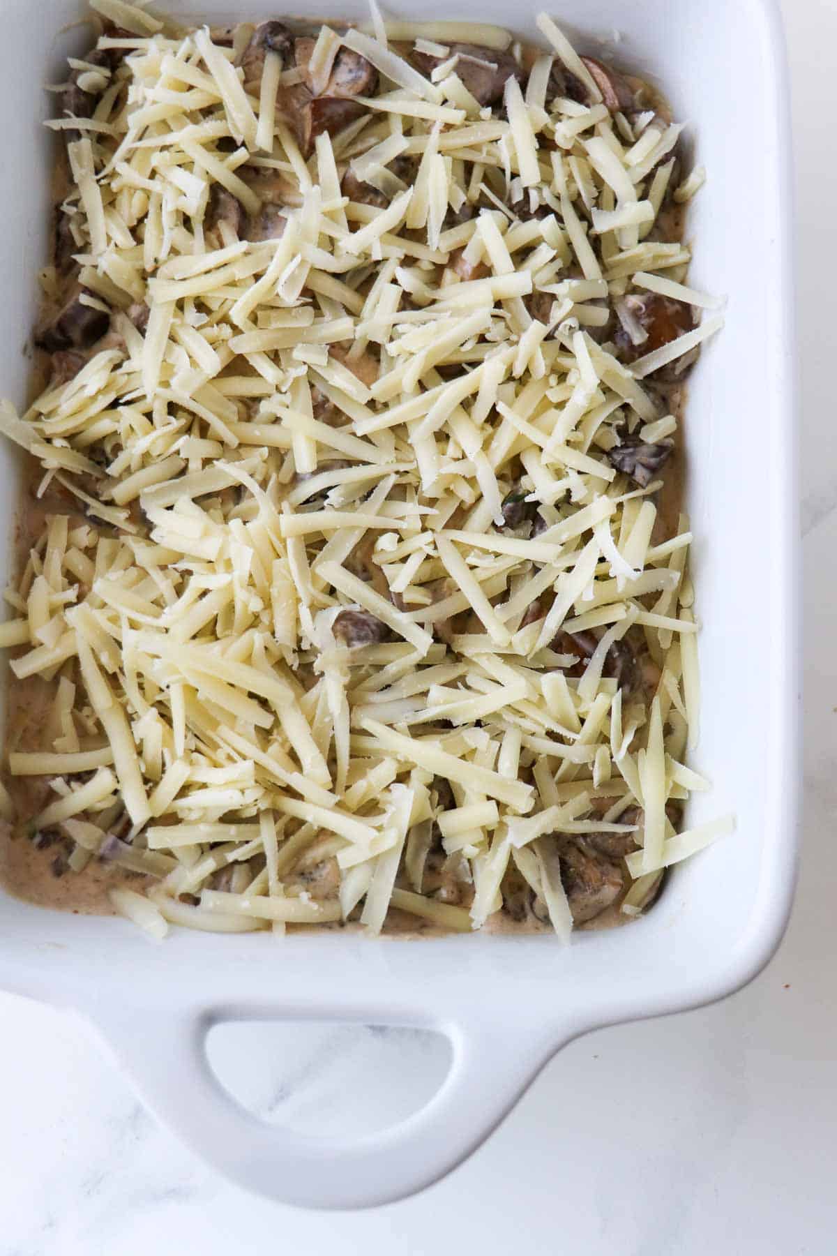 Creamy mushrooms in a baking dish topped with shredded cheese.