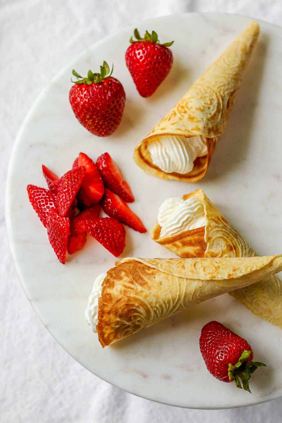 Krumkake filled with whipped cream next to fresh strawberries.