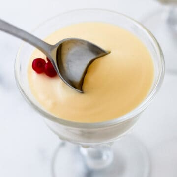 Close up of a spoon in a serving of Swedish Cream topped with lingonberries.