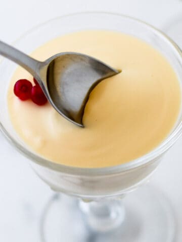 Close up of a spoon in a serving of Swedish Cream topped with lingonberries.