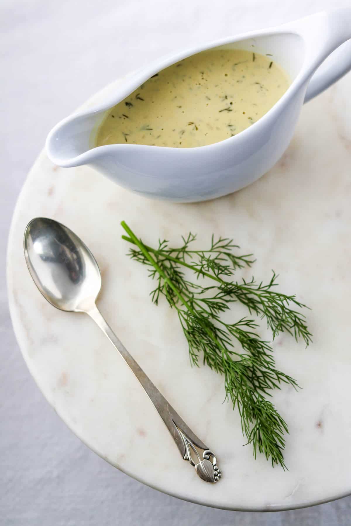 Warm Mustard Dill Sauce in a gravy boat next to a spoon and a sprig of dill.