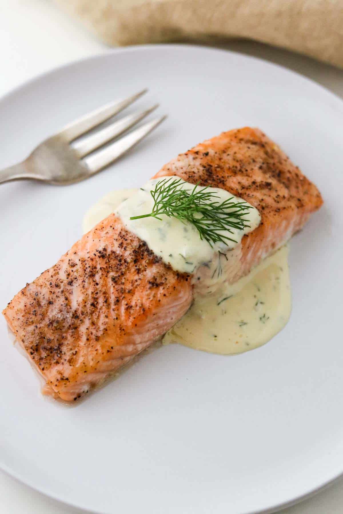Baked salmon on a plate topped with Warm Mustard Dill Sauce.