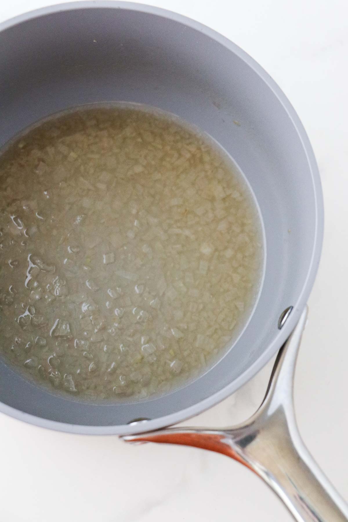 Minced shallots and wine cooking in a gray saucepan.