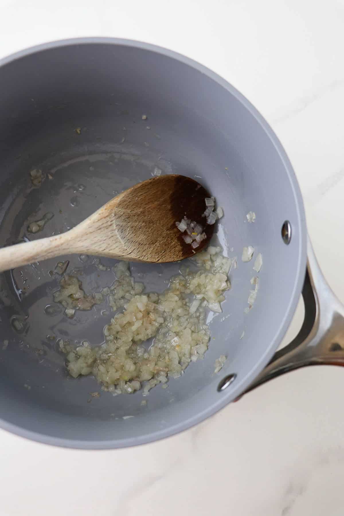 Cooked minced shallots in a saucepan with a wooden spoon.