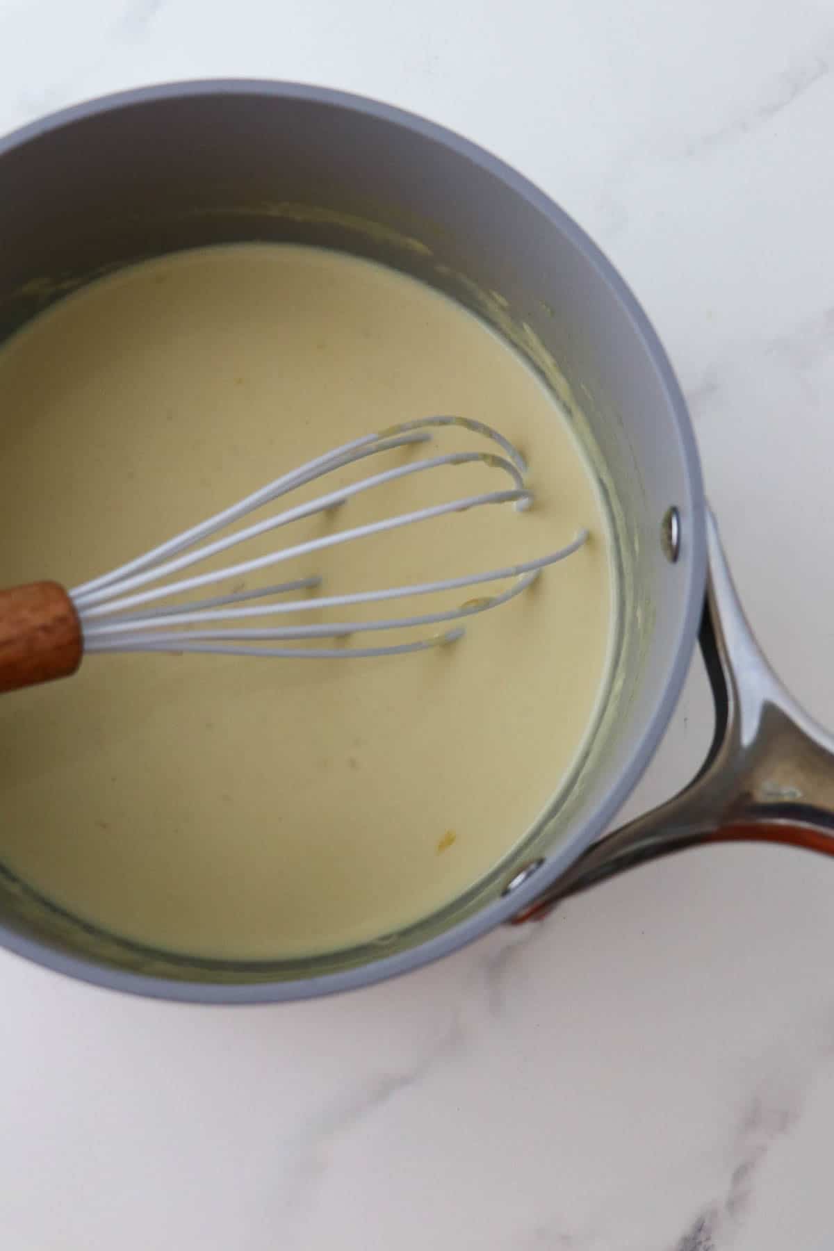 Mustard sauce in a saucepan with a whisk.