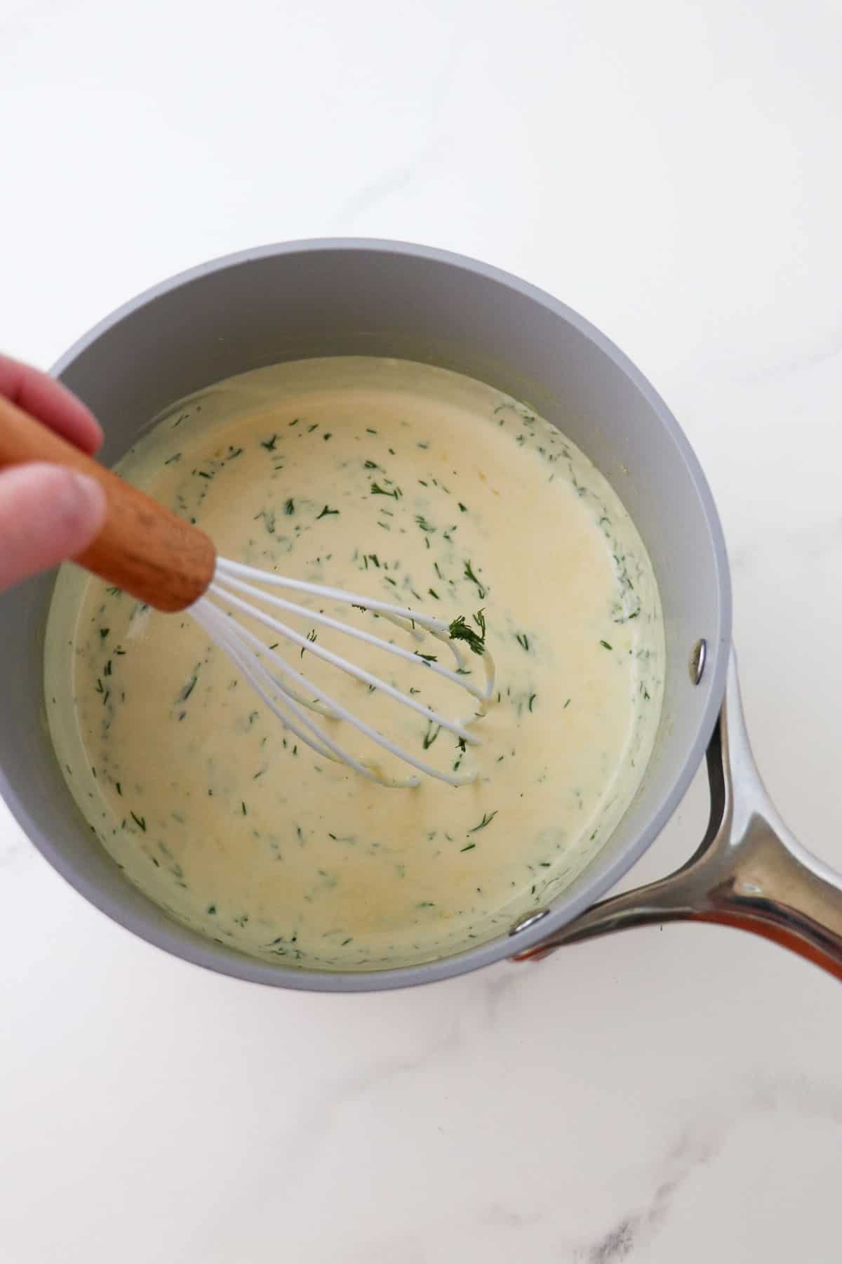 Warm Mustard Dill Sauce in a gray saucepan with a whisk.