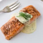 Close up of baked salmon topped with Warm Mustard Dill Sauce and a sprig of dill.