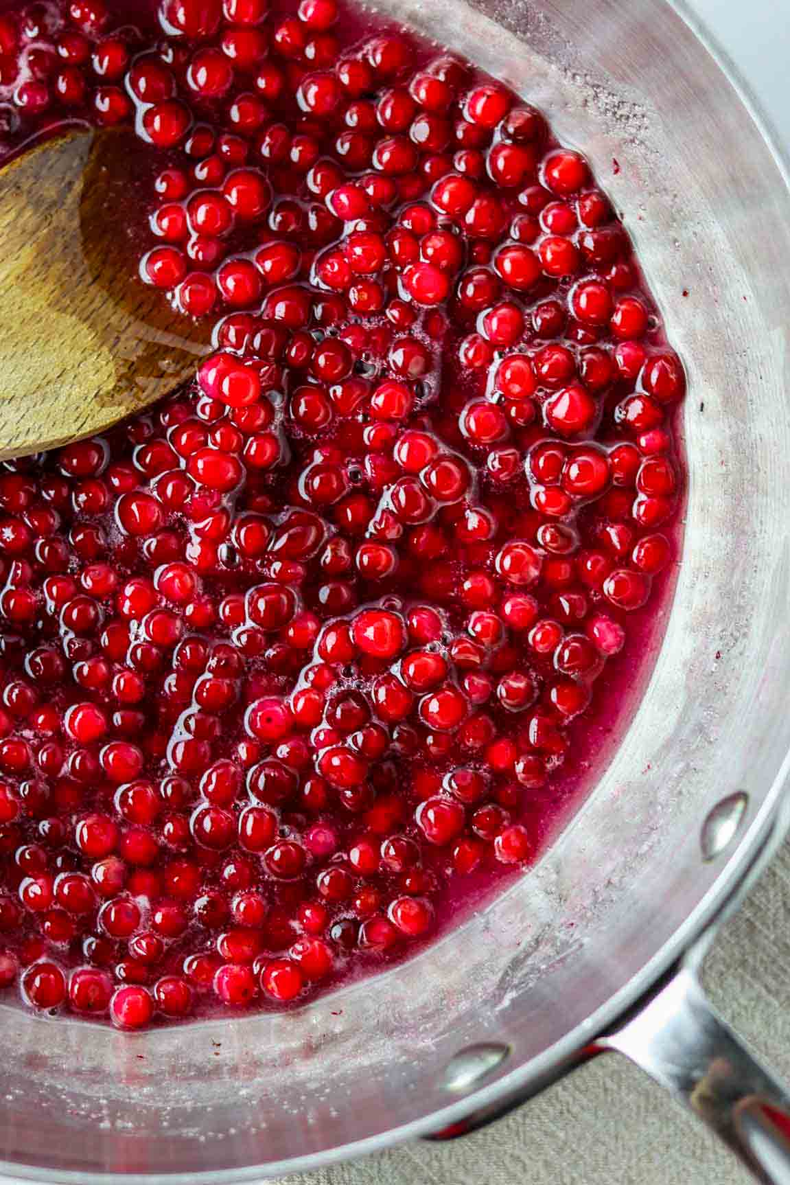 Lingonberries in a metal saucepan with a wooden spoon.