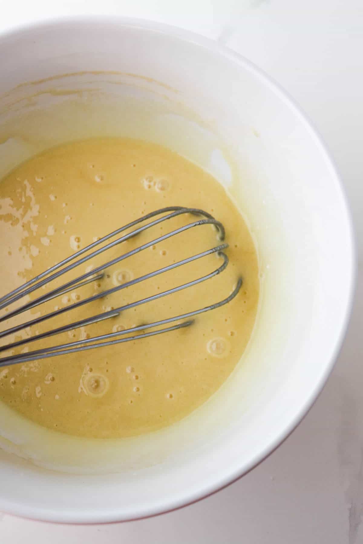 Eggs, sugar, oil and vanilla extract whisked together in a white bowl.