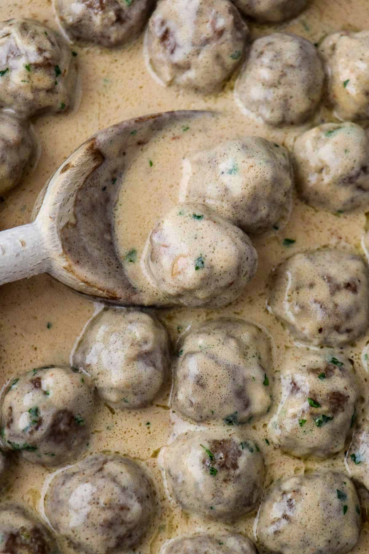 Close up of Swedish meatballs in sauce with a wooden spoon.