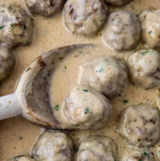 Close up of Swedish meatballs in sauce and a wooden spoon.