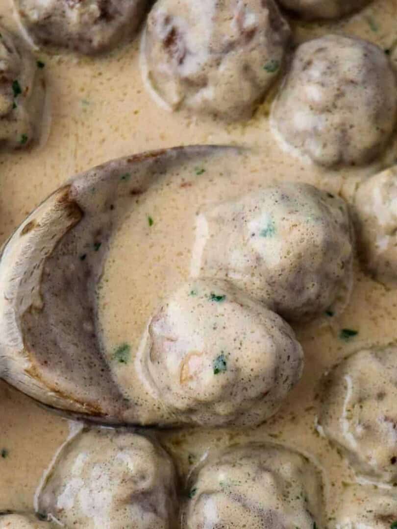 Close up of Swedish meatballs in sauce and a wooden spoon.
