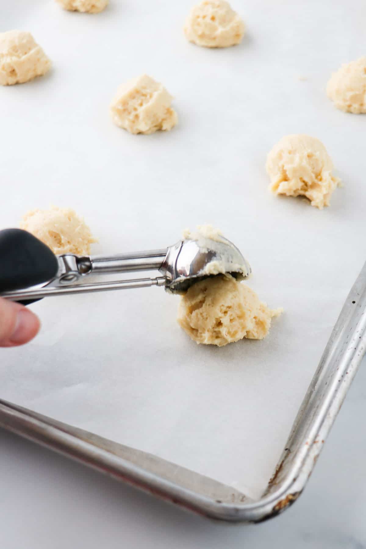Person scooping Old-Fashioned Buttermilk cookie dough onto a baking sheet with metal scoop.