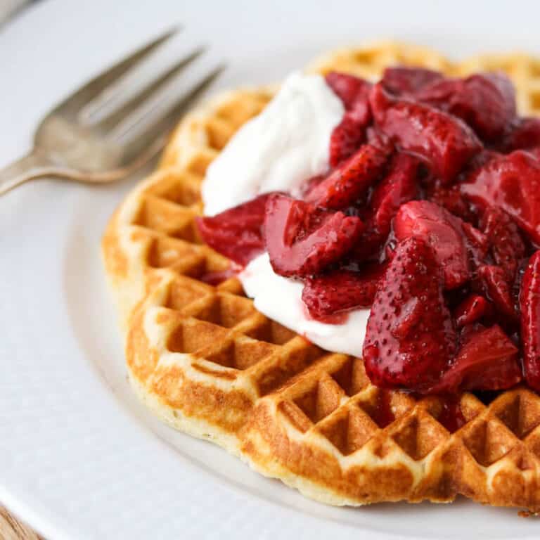 Close up of waffle topped with roasted strawberries and whipped cream.