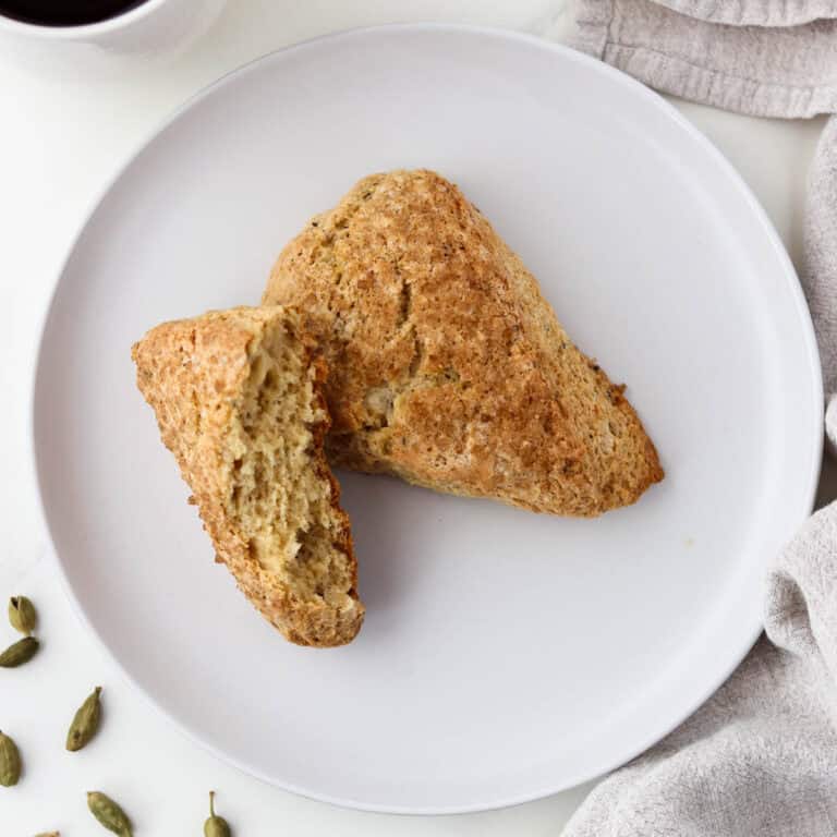 Brown Sugar Cardamom Scones on a white plate next to cardamom pods.