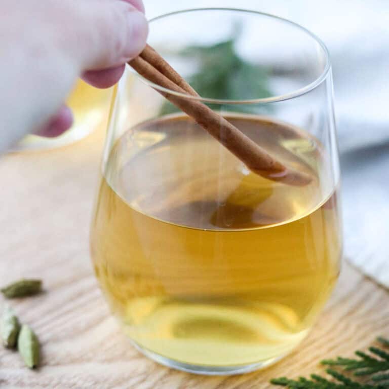 Glass of white glögg (mulled white wine) being stirred with a cinnamon stick.