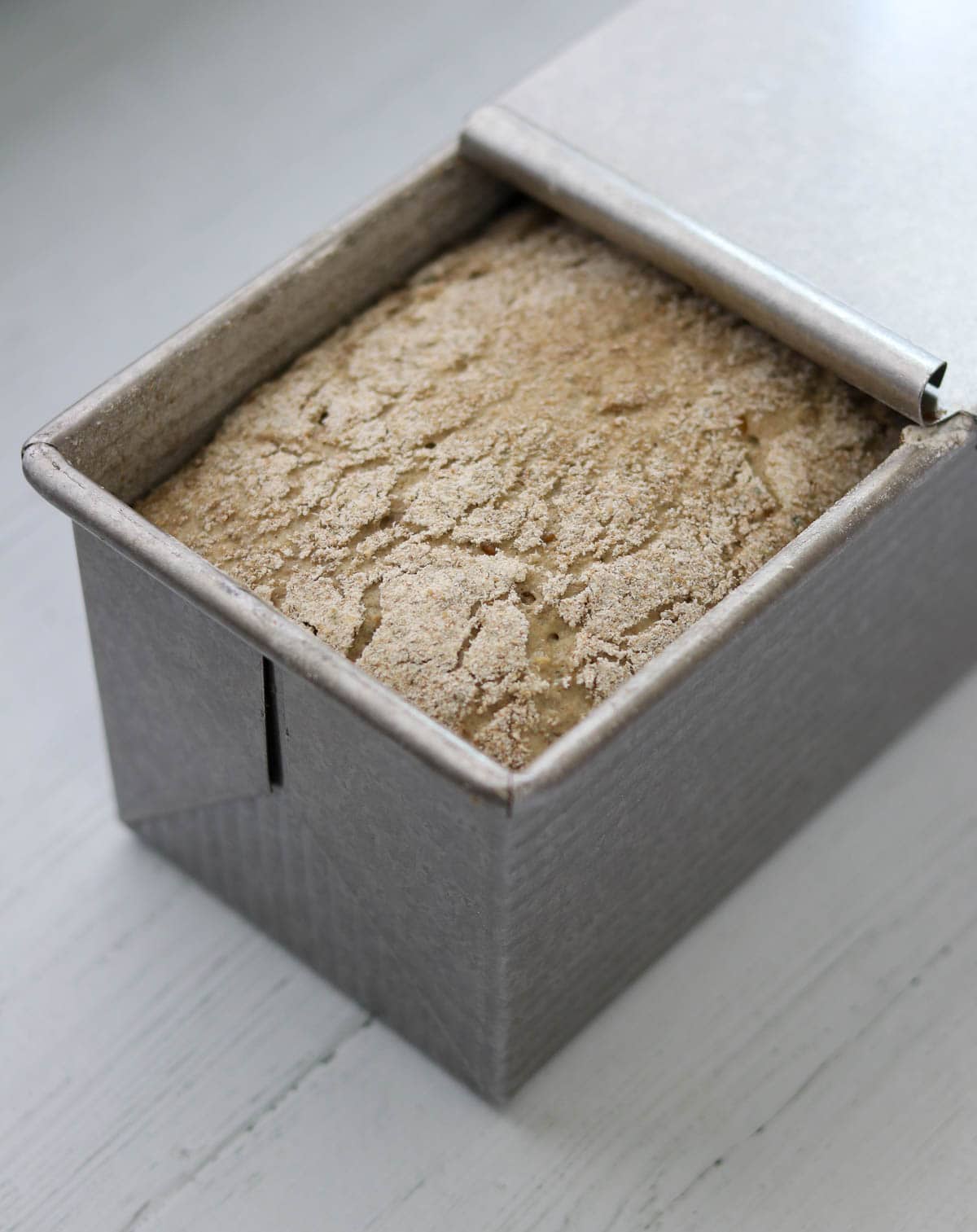 Danish Rye Bread rising in a pullman pan with the lid partially removed.