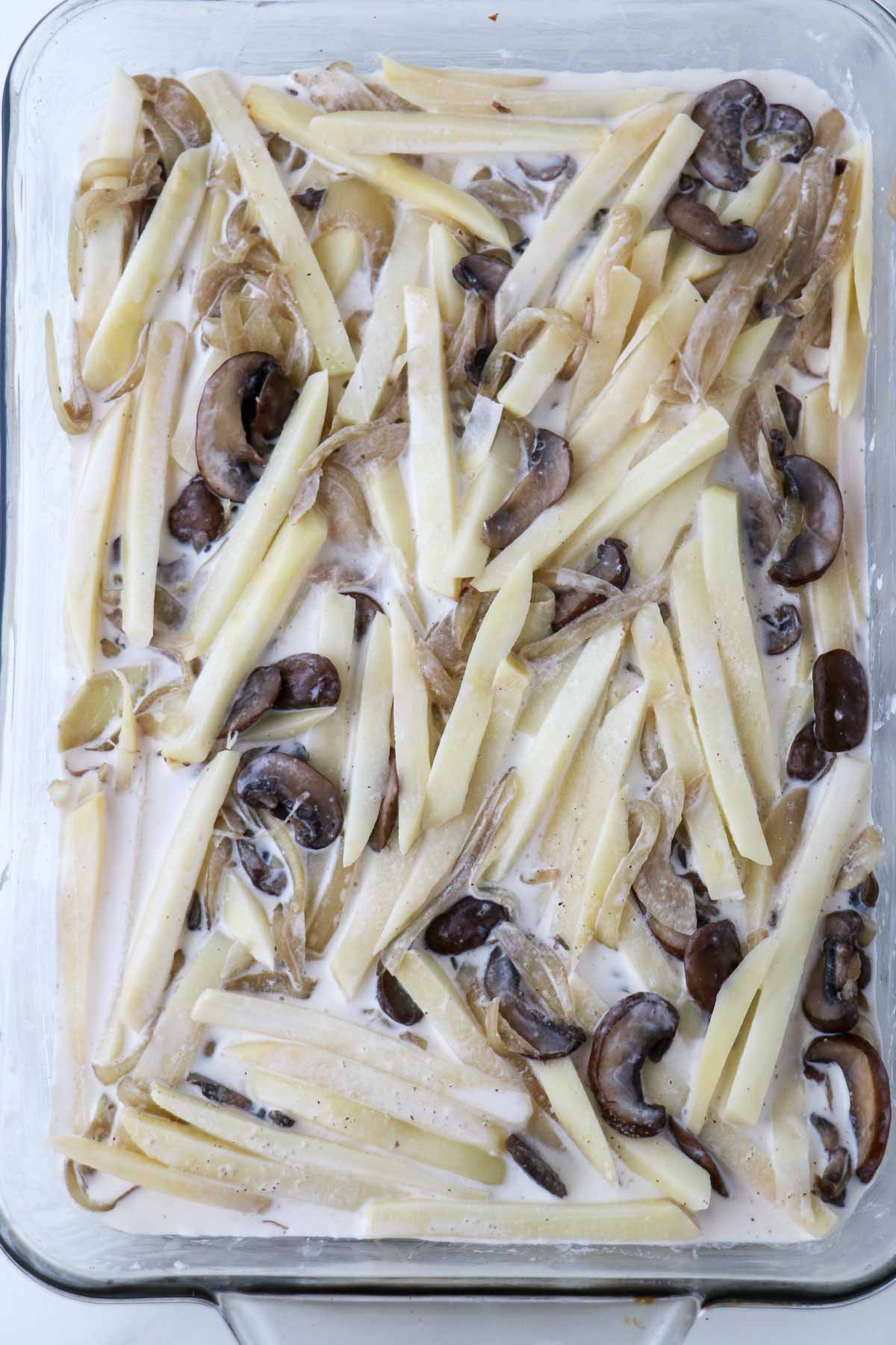 Sliced potatoes, mushrooms, onions and cream layered in a glass baking dish.