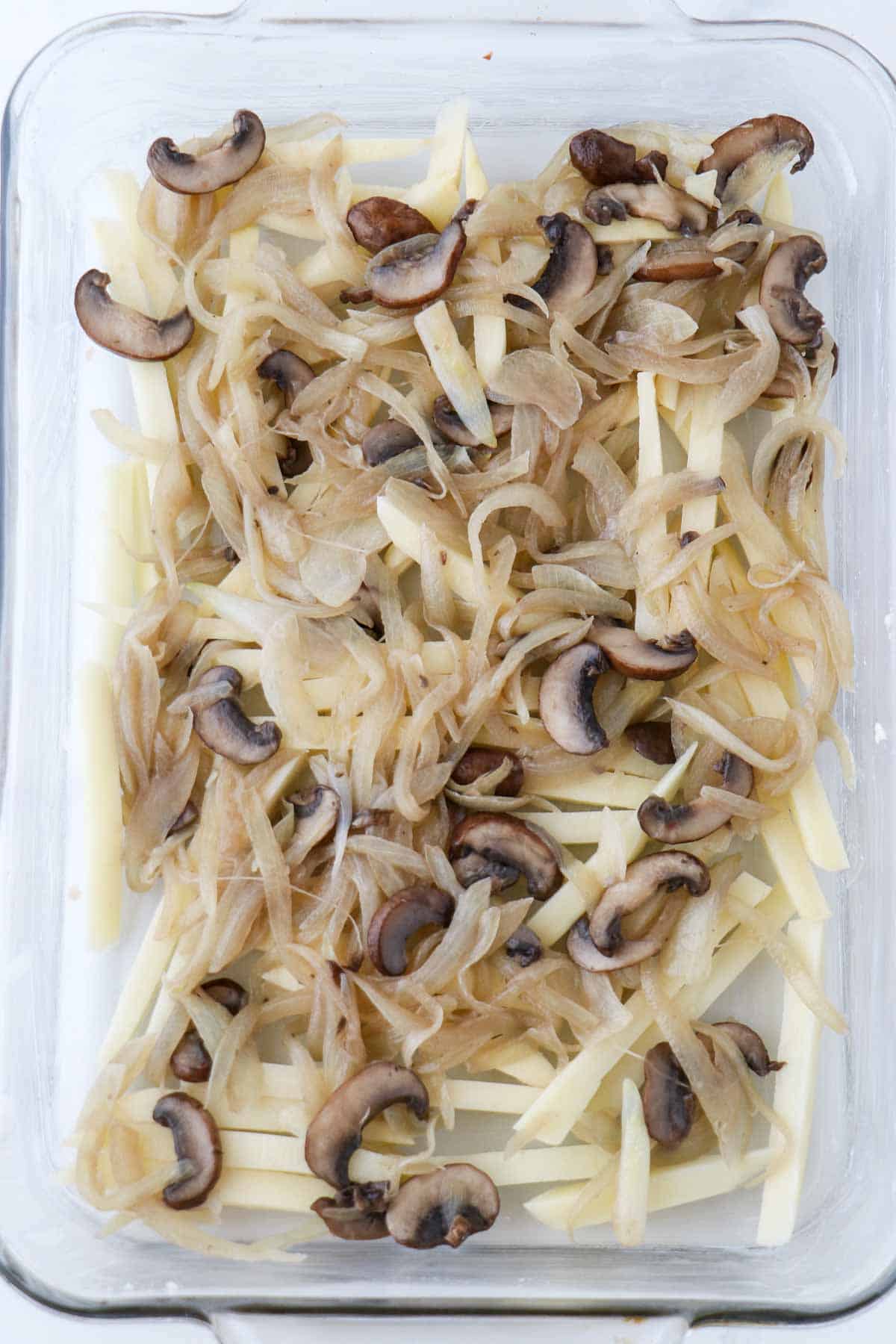 Sliced potatoes topped with cooked mushrooms and onions in a glass baking dish.