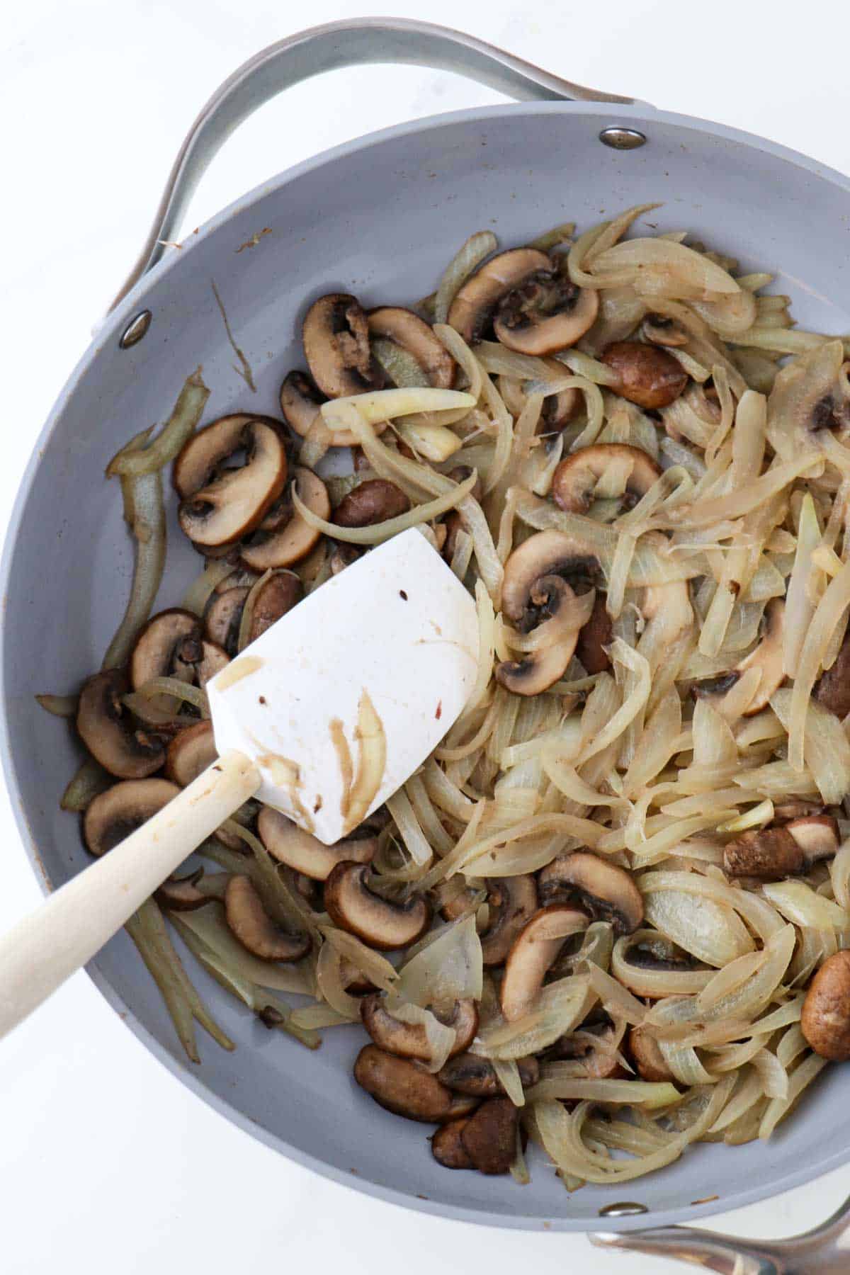 Cooked onions and mushrooms in a skillet a with a rubber spatula.