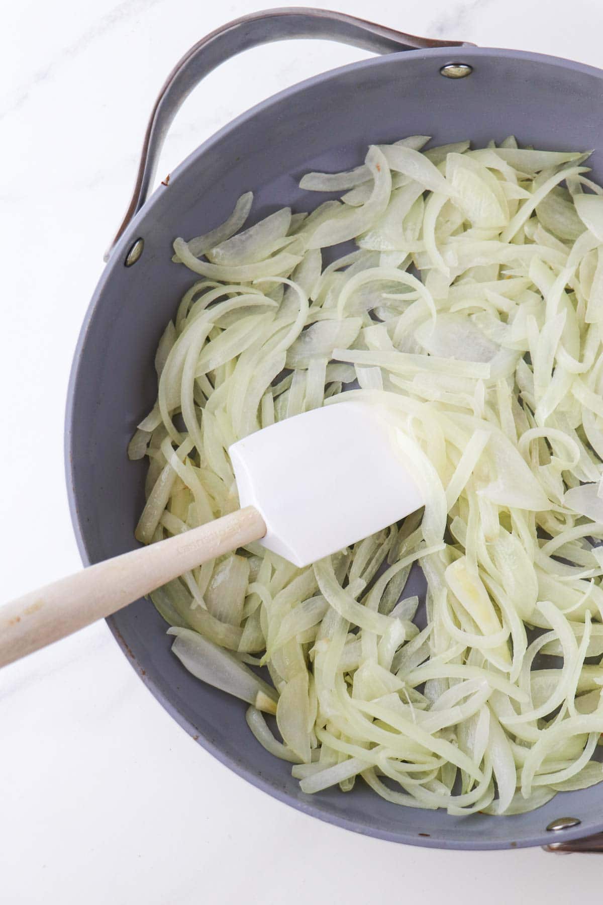 Cooked onions in a skillet with a rubber spatula.