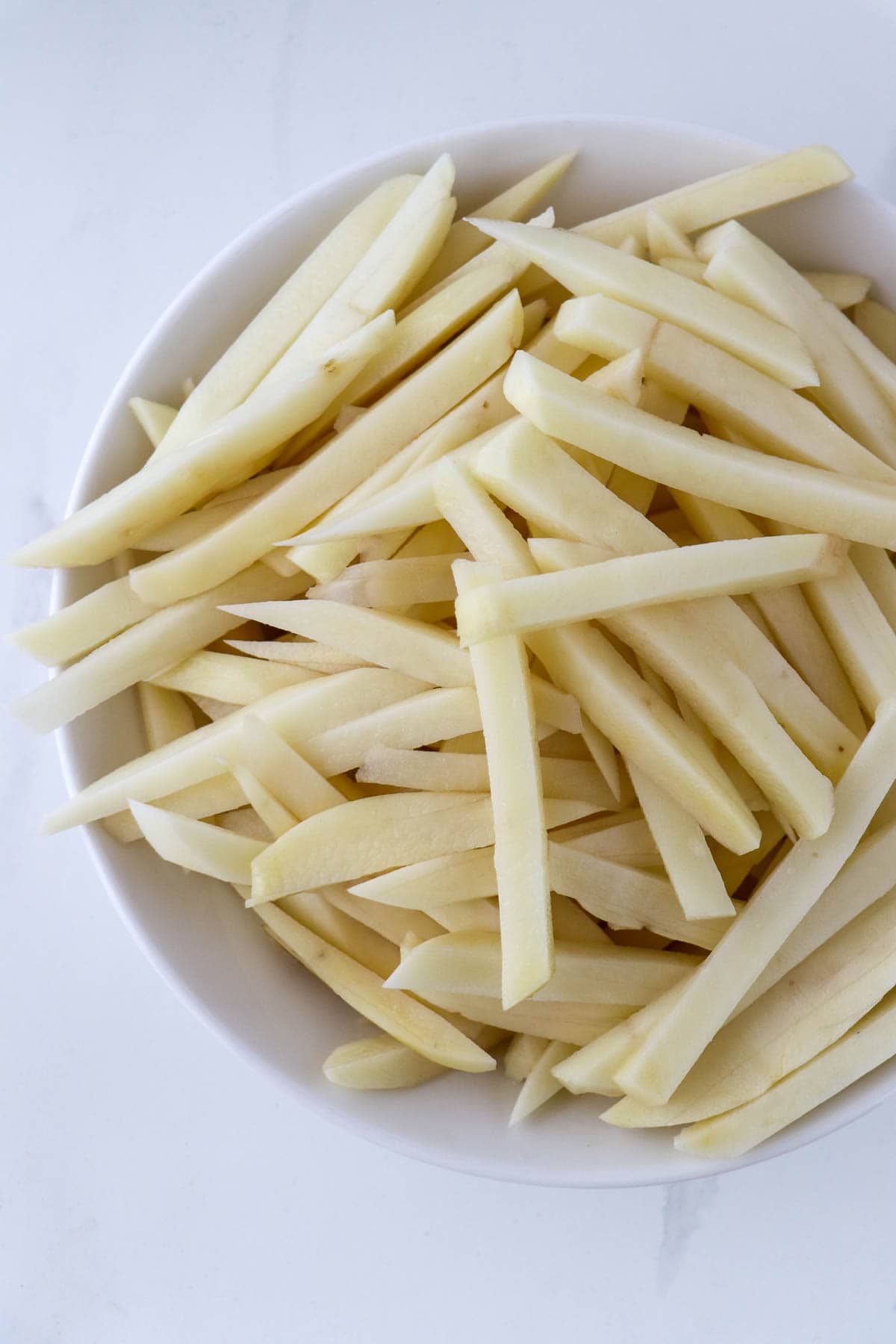 Uncooked sliced potatoes in a white bowl.