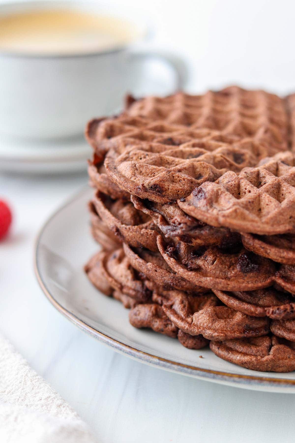 Stack of Chocolate Waffles on a plate next to a cup of coffee.