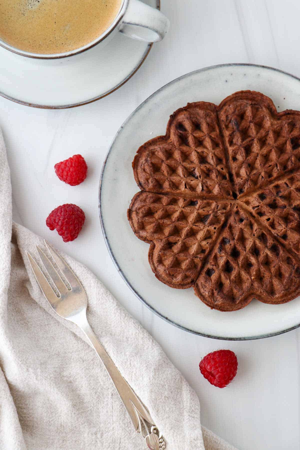 Scandinavian-Style Chocolate Waffle on a plate next to raspberries, coffee and a fork.