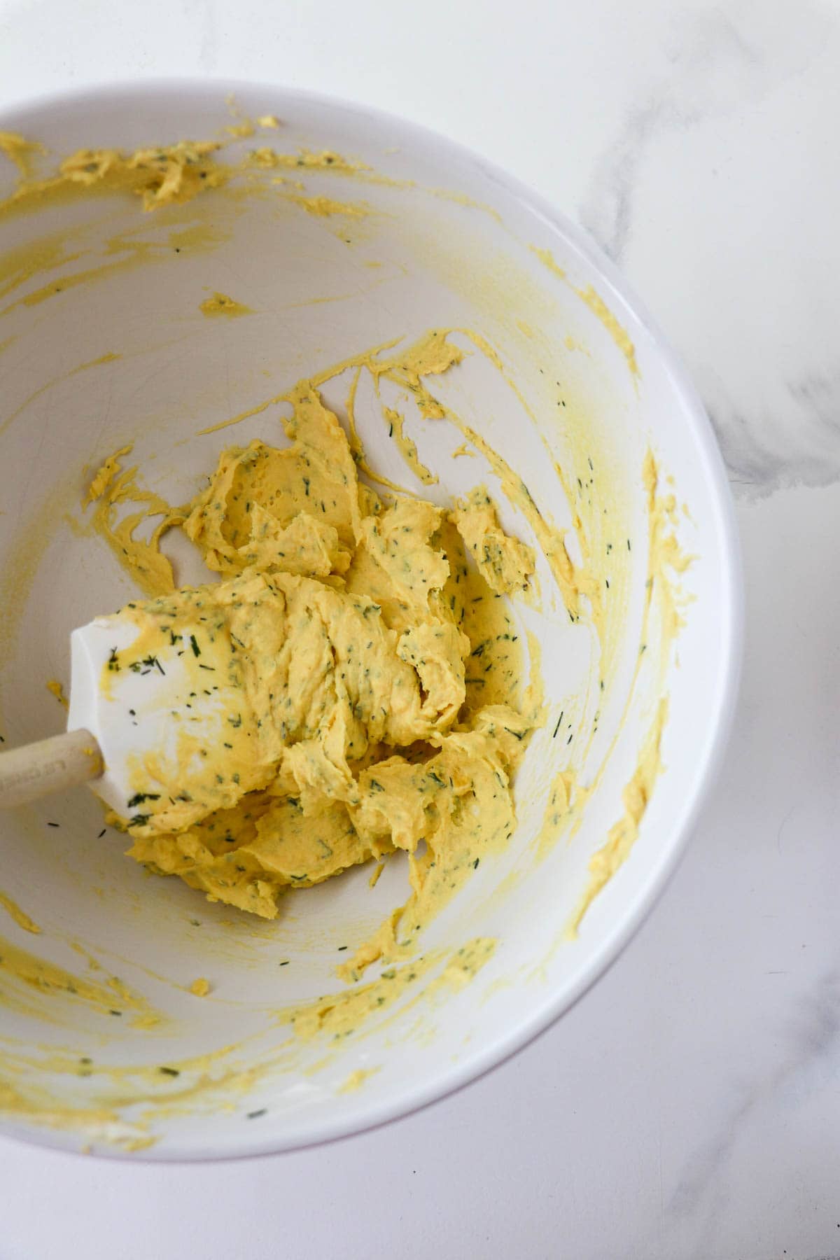 Deviled Eggs with Dill filling in a white bowl with a rubber spatula.