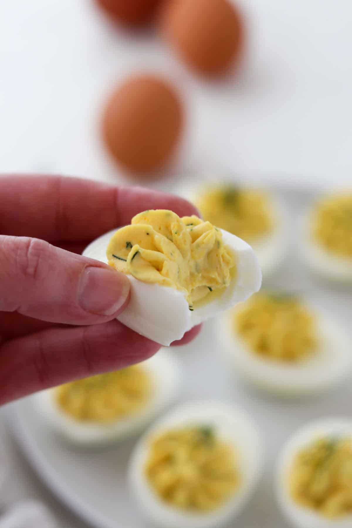 Person holding a deviled egg with a bite out of it.