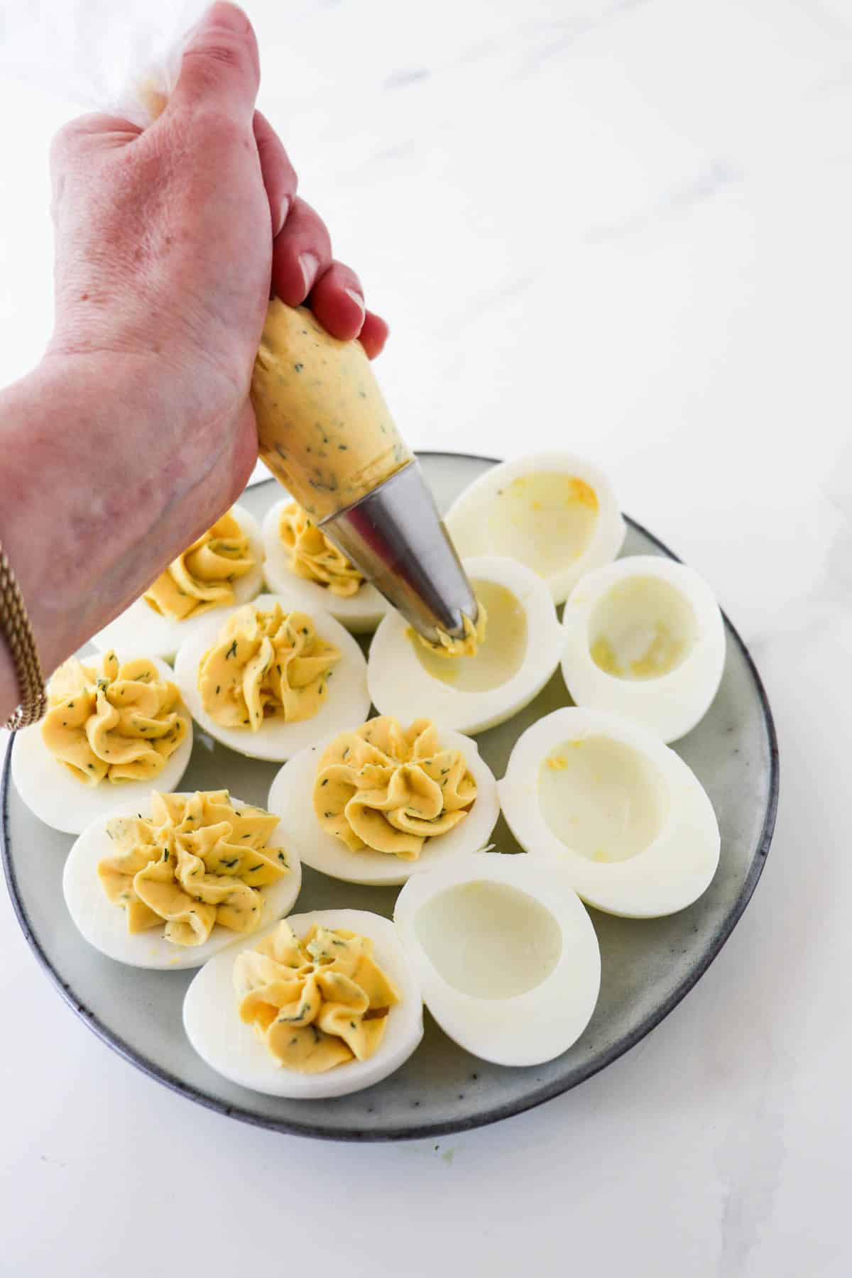 Person piping deviled egg filling into egg white halves.