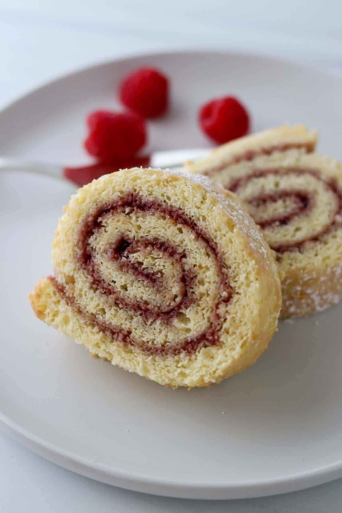 Two slices of Swedish Rulltårta on a plate with raspberries and a fork.